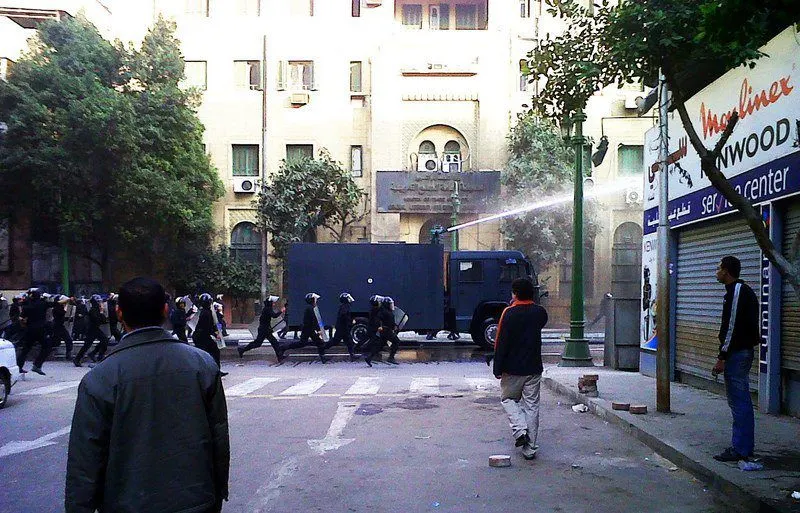 Riot police with sticks and fire hoses run by to stop protesters.